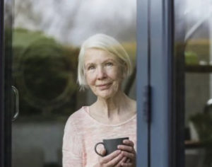 senior woman standing alone looks out window