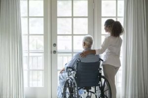 young caregver and senior patient in wheelchair gazing out window copy