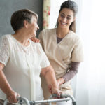 Young female caregiver helping senior lady with walker