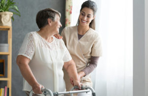 Young female caregiver helping senior lady with walker