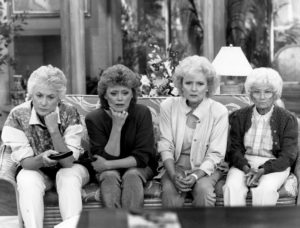 All the stars of "The Golden Girls" TV show sitting on a couch, leaning in to watch TV