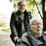 older woman pushing senior man in wheelchair