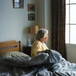 senior woman sitting on bed looking out window