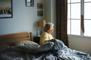 senior woman sitting on bed looking out window