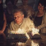 senior man blowing out dozens of birthday candles