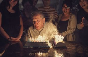 senior man blowing out dozens of birthday candles